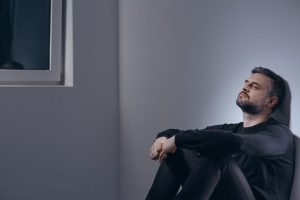 Sad man sits against wall battling mental illness.